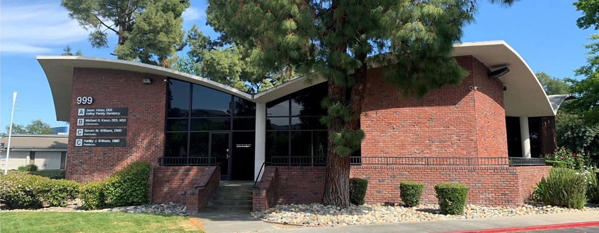 Brick dental office building with entrance, landscaping, and clear signage under blue sky.
